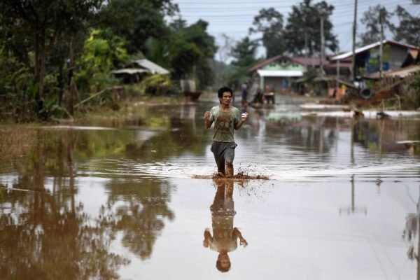 LAOS-DAM-DISASTER-ACCIDENT A man wades through a flooded road at a village in Sanamxai, Attapeu province, on July 26, 2018.
Rescuers battled fresh rains on July 26 to reach scores of people still missing after a dam collapse in southern Laos that unleashed a torrent of water, washing away whole villages and killing at least 26 people. / AFP PHOTO / NHAC NGUYEN