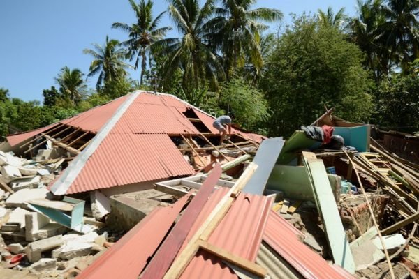 INDONESIA-QUAKE A man walks over the roof of a collapsed house at Pemenang village in northern Lombok in West Nusa Tenggara province on August 7, 2018, two days after the area was struck by an earthquake.
The shallow 6.9-magnitude quake killed at least 105 people and destroyed thousands of buildings in Lombok on August 5, just days after another deadly tremor surged through the holiday island and killed 17. / AFP PHOTO / SONNY TUMBELAKA